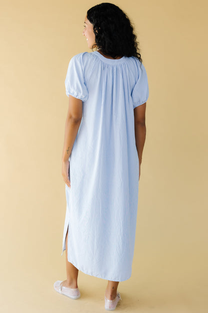 Back view of a woman wearing a light blue  plaid midi dress with side slits with large puff sleeves.