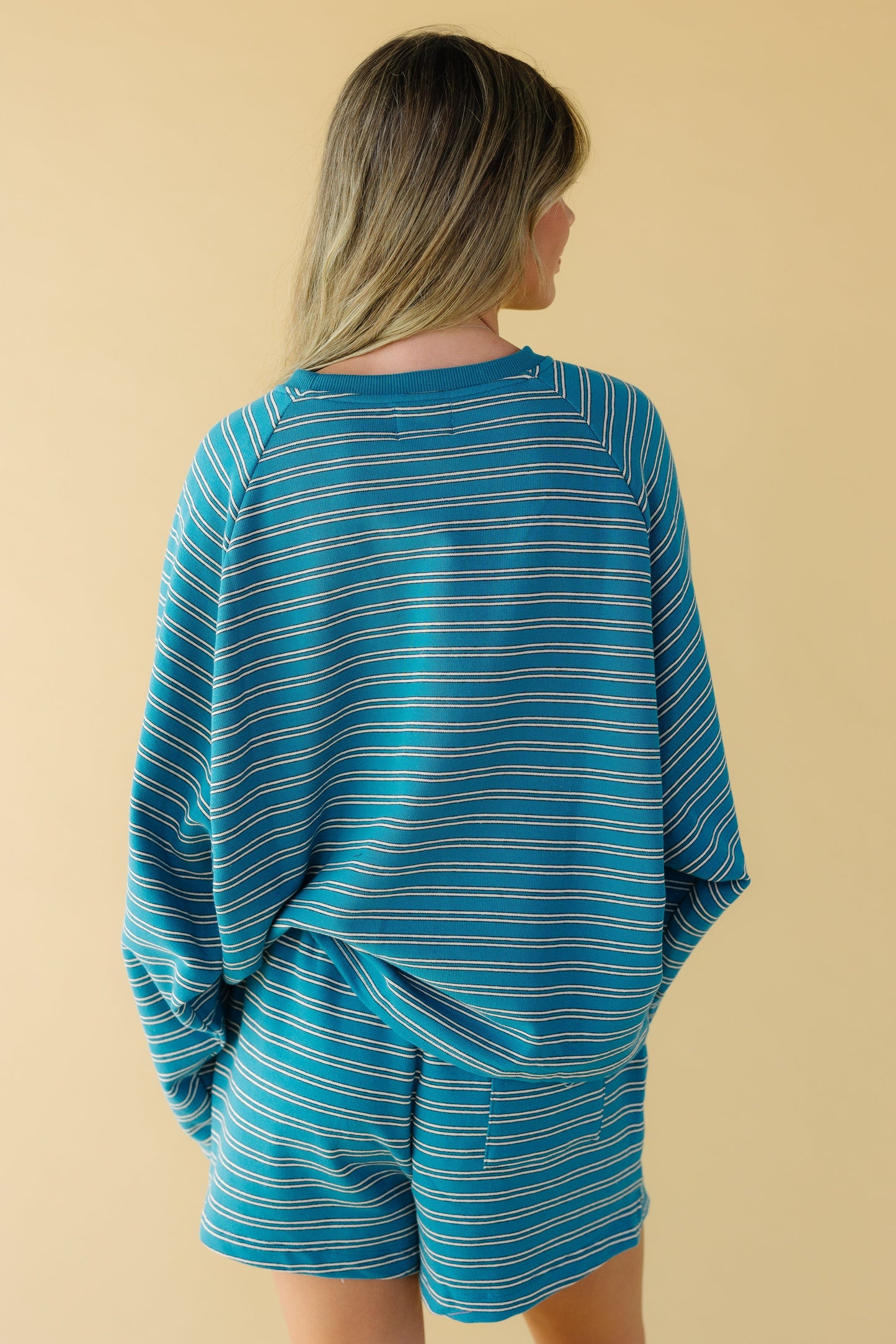 Back view of a woman wearing a teal stripe, loose fitting stripe short set with long sleeves.