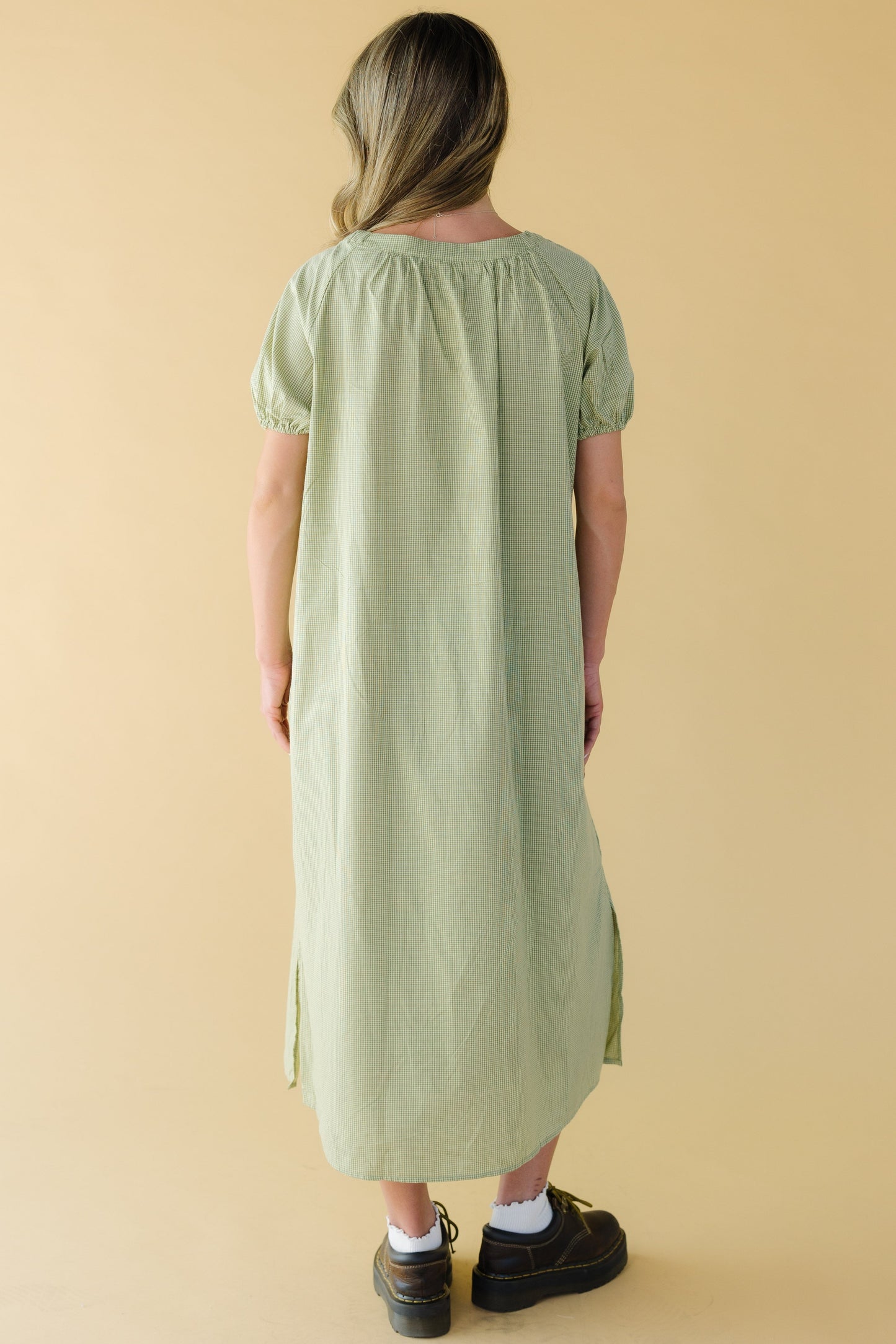 Back view of a young woman wearing a green gingham midi dress with large puff sleeves.