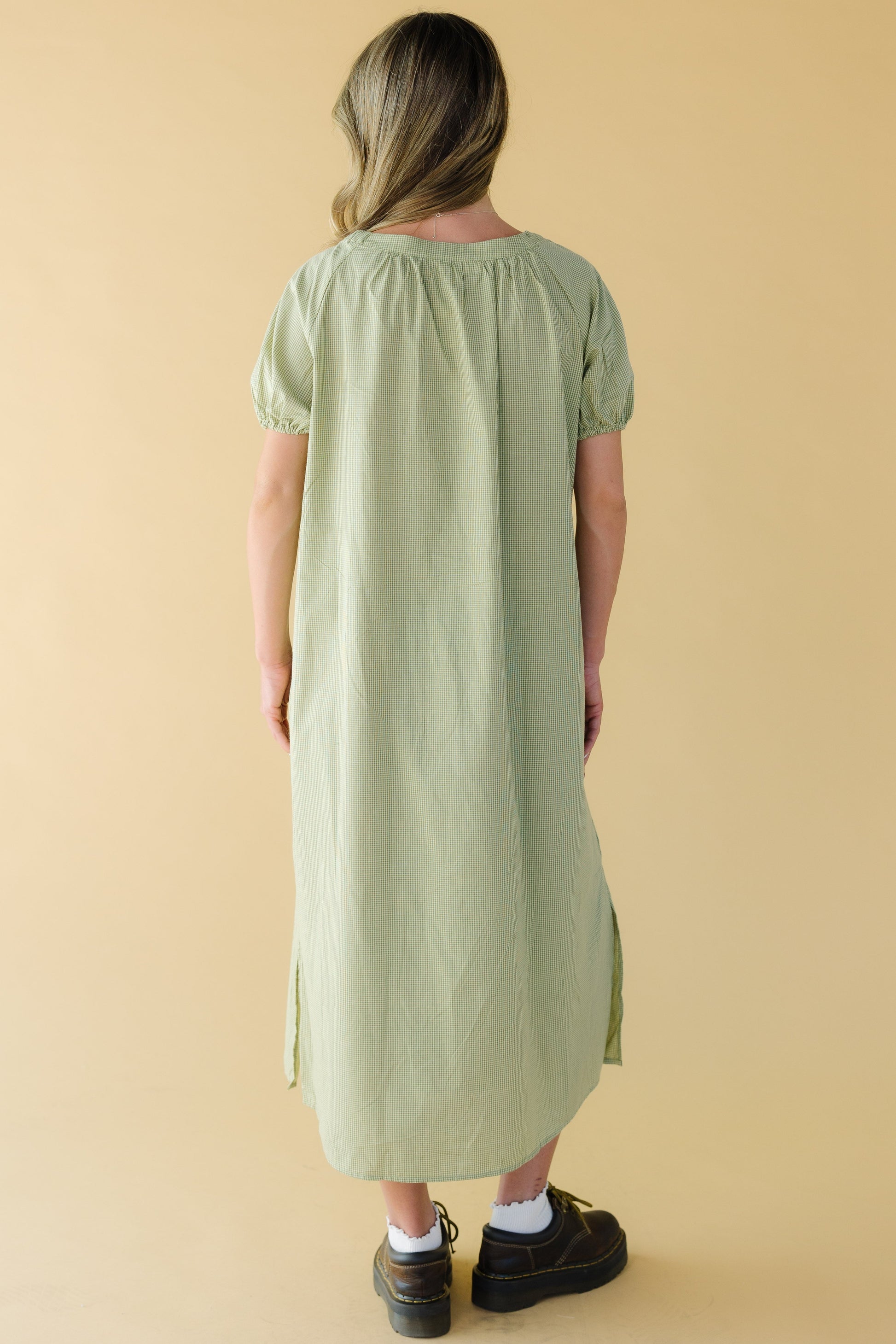 Back view of a young woman wearing a green gingham midi dress with large puff sleeves.