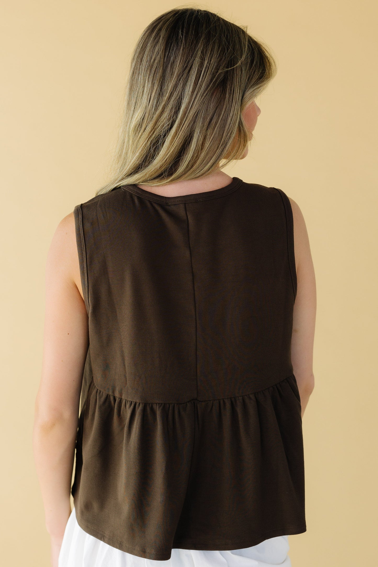 Back view of a young woman wearing a sleeveless bronw loose fitting top.