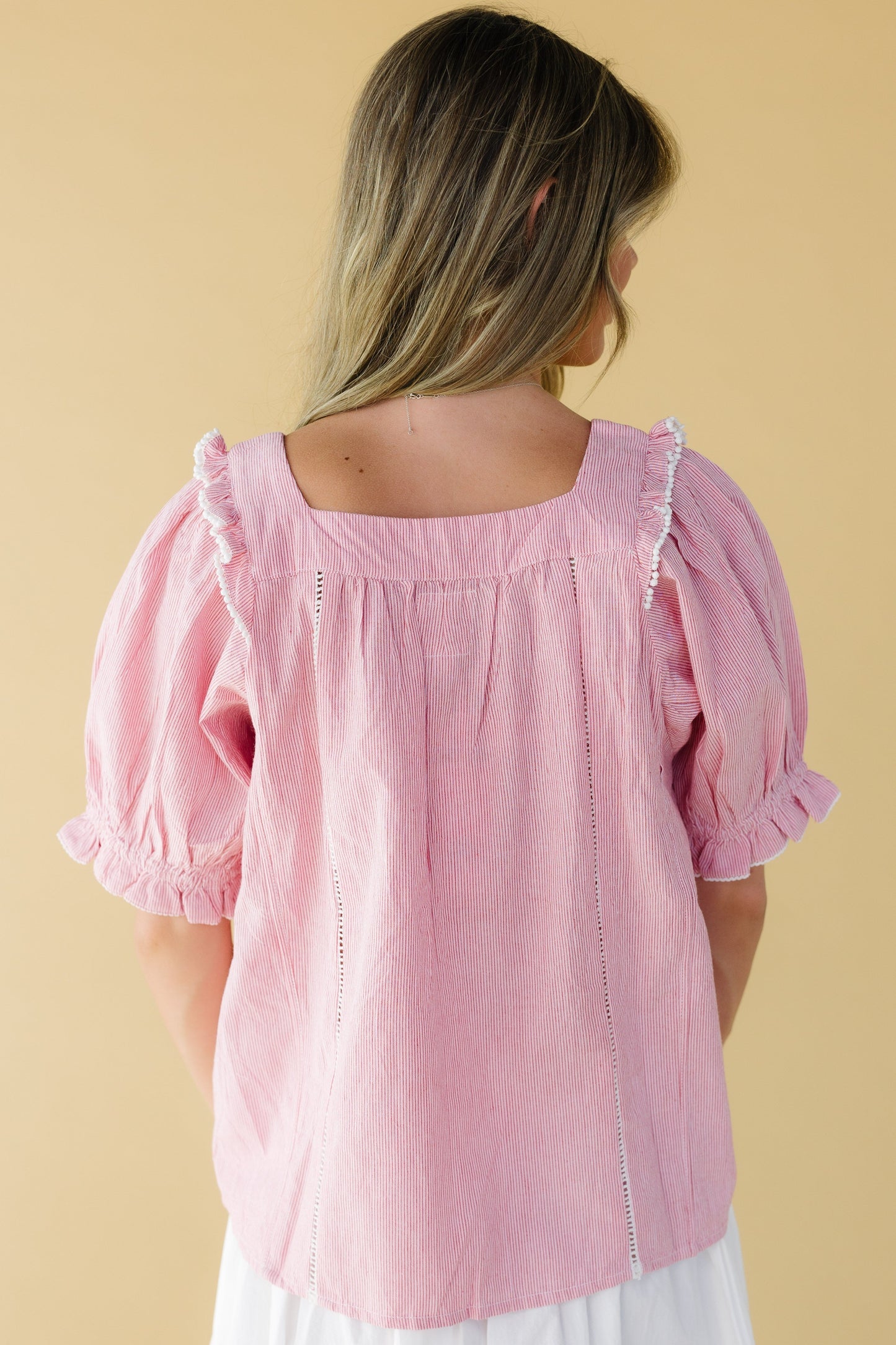 Back view of a woman wearing a loose fitting red & white stripe top with a square neckline and elbow length puff sleeves.