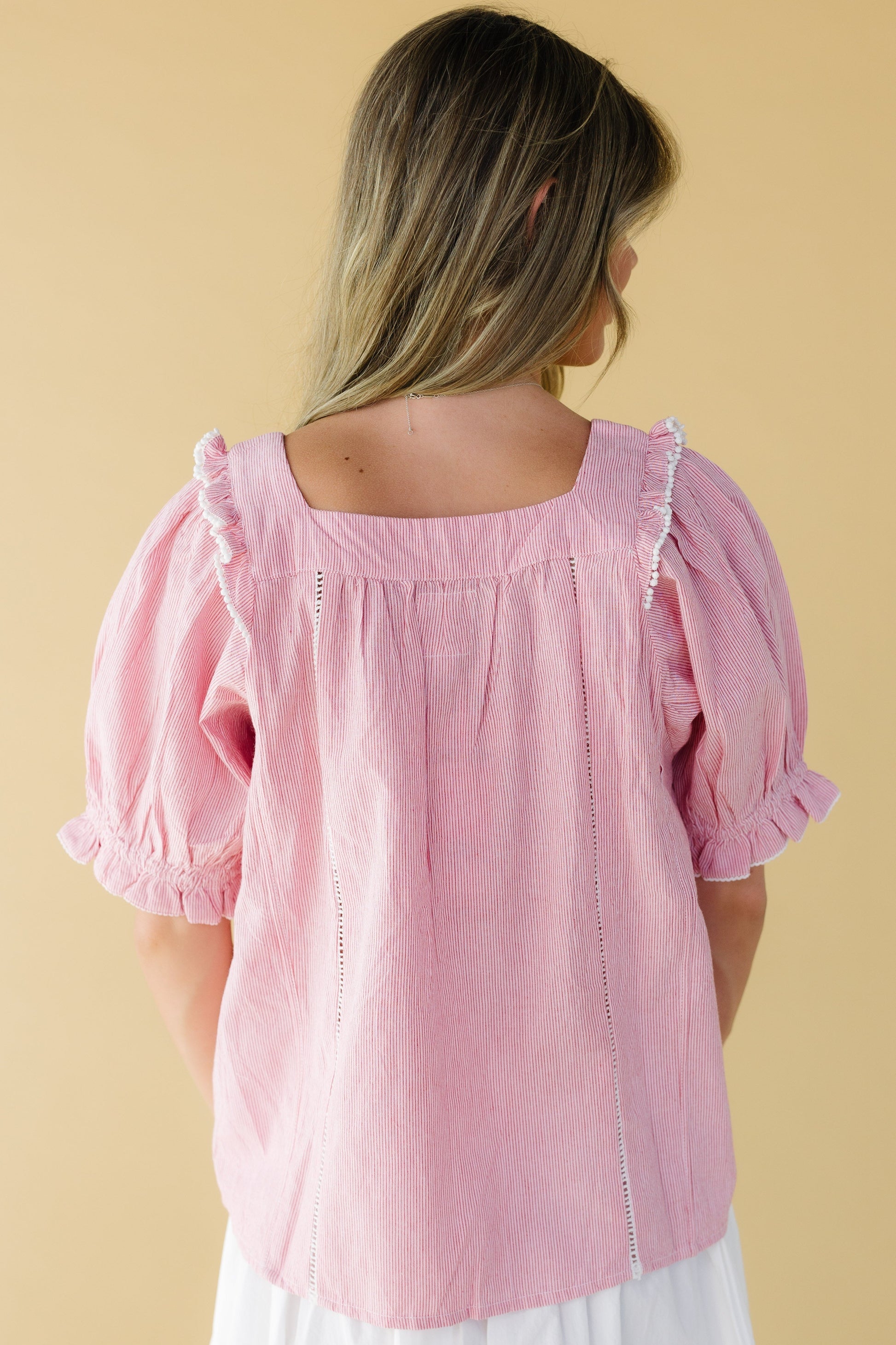 Back view of a woman wearing a loose fitting red & white stripe top with a square neckline and elbow length puff sleeves.