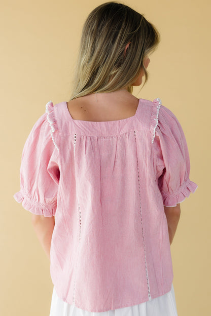 Back view of a woman wearing a loose fitting red & white stripe top with a square neckline and elbow length puff sleeves.