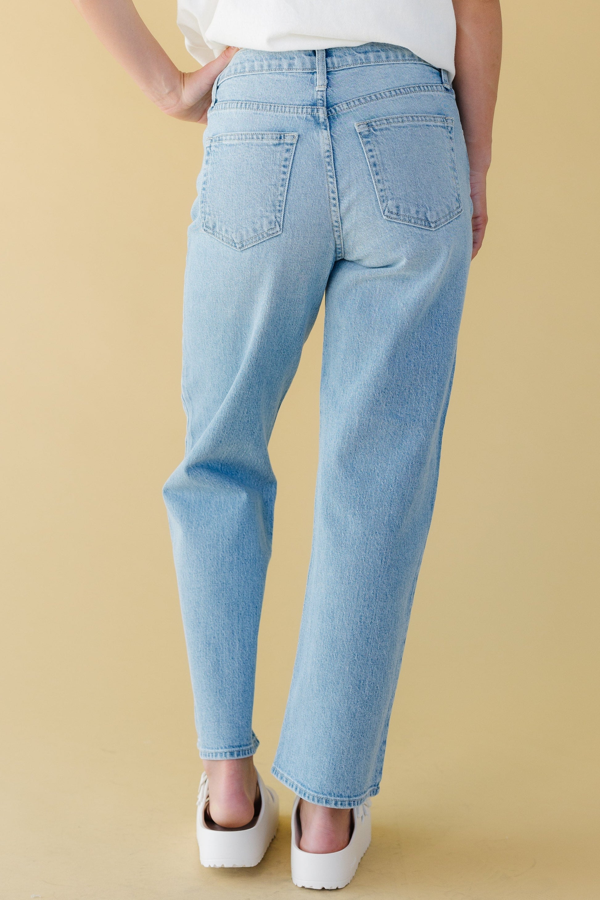 Back view of a young woman wearing a pair of light denim straight leg jeans.