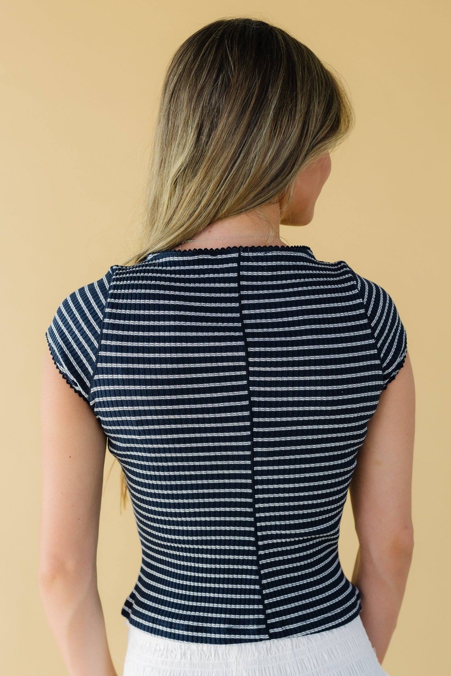 Back view of a woman wearing a navy stripe, close fitting stripe top with cap sleeves.