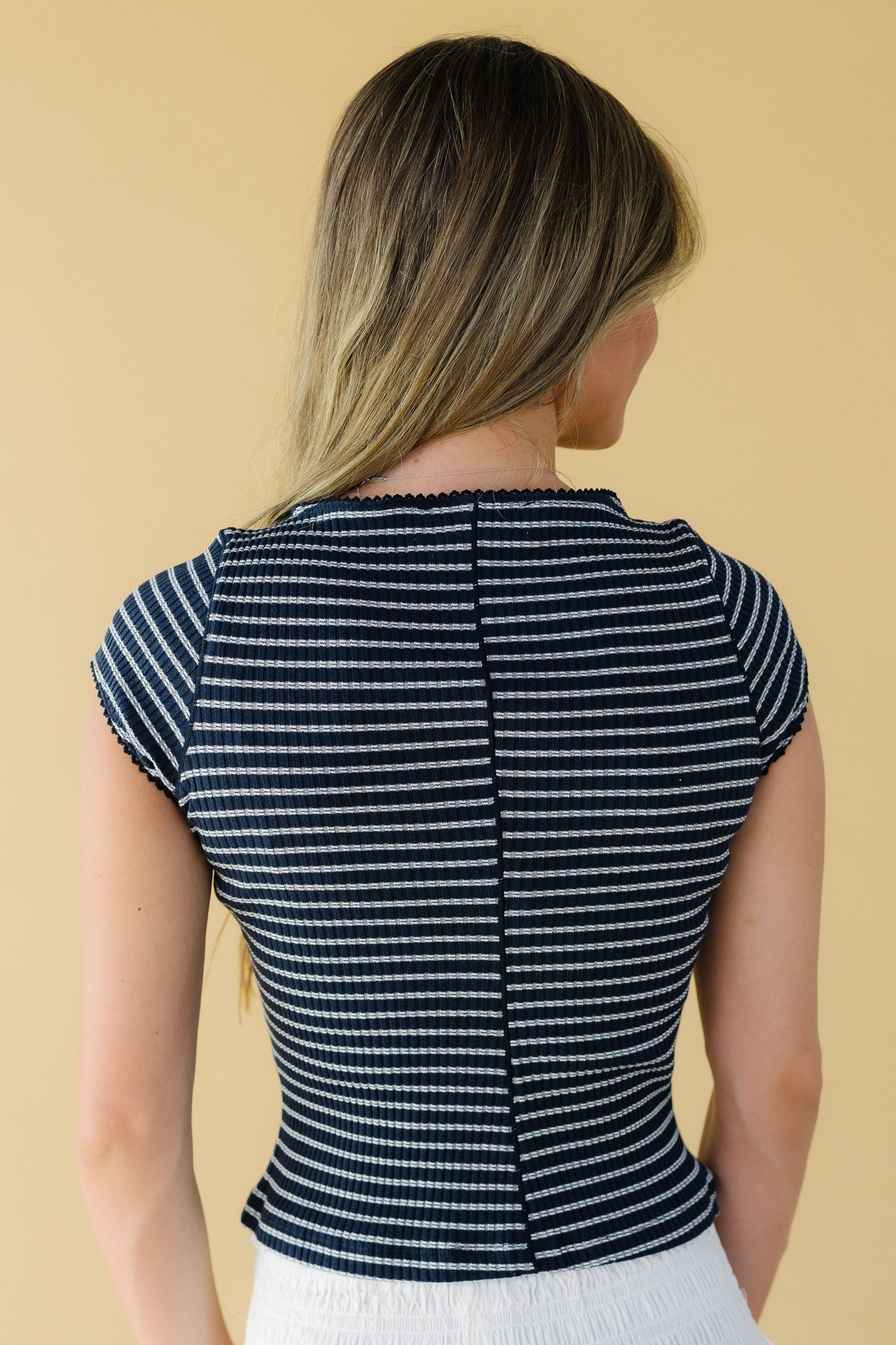 Back view of a woman wearing a navy stripe, close fitting stripe top with cap sleeves.