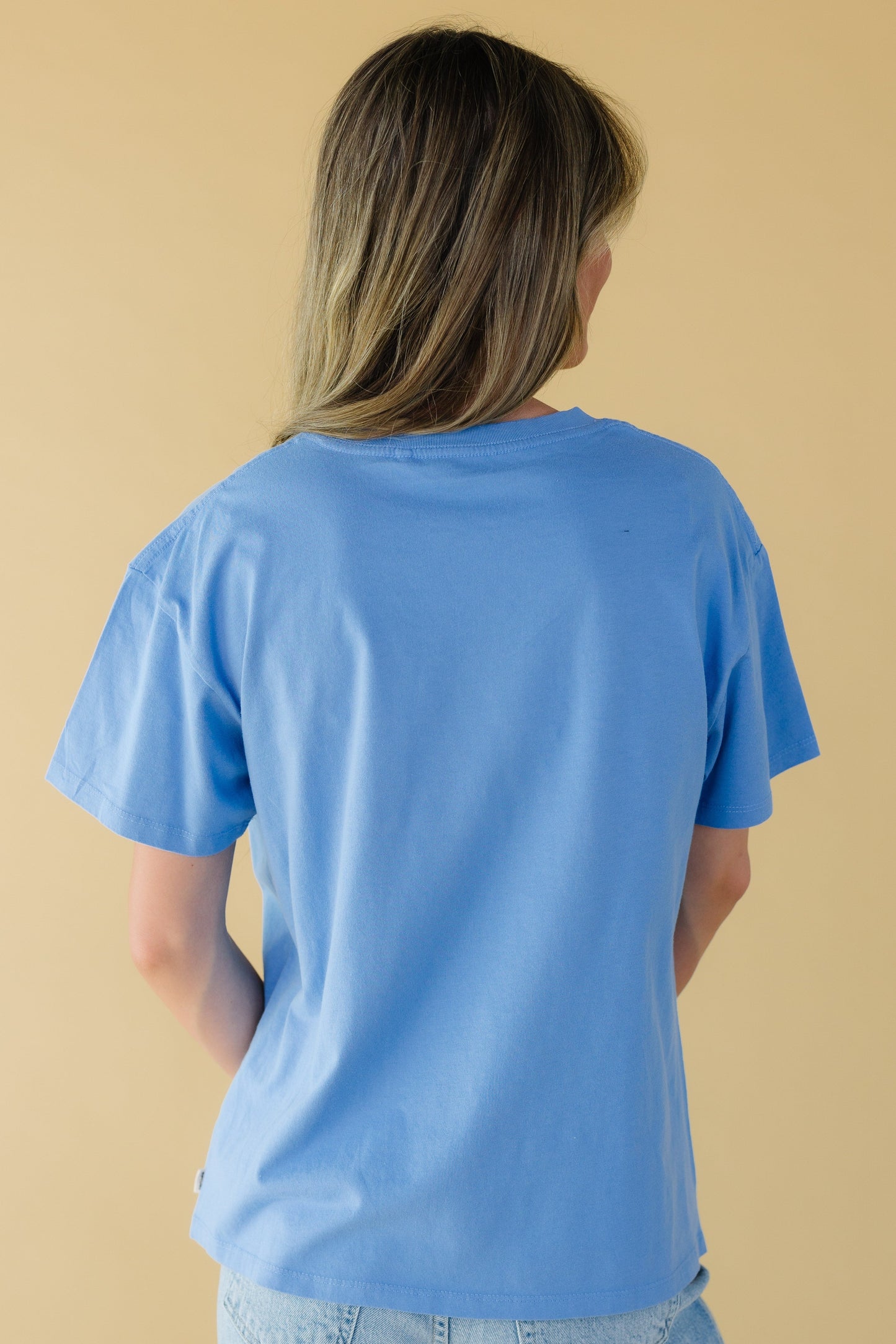 Back view of a young woman wearing a blue short sleeve tee.