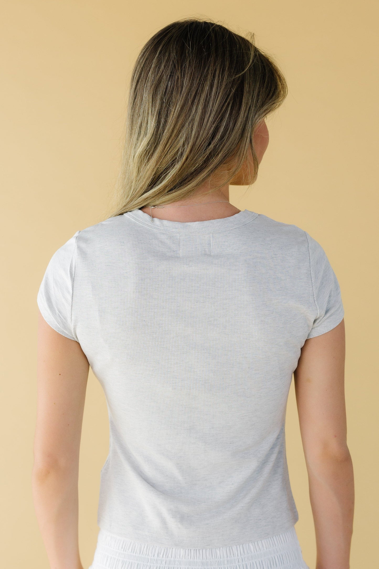 Back view of a woman wearing a grey rib knit top with short sleeves.