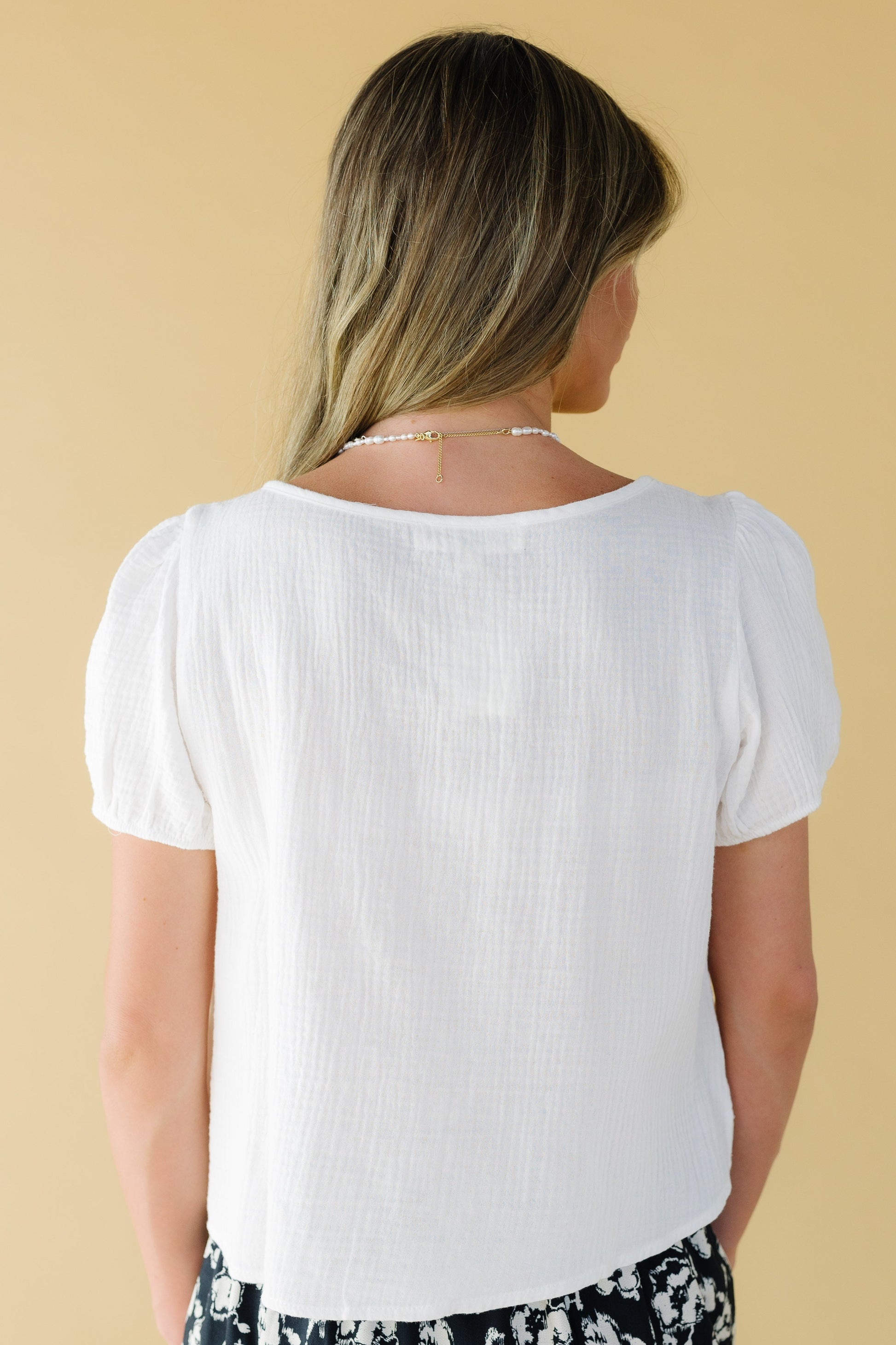 Back view of a woman wearing a white crepe textured blouse with short sleeves.