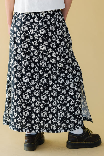 Back view of a young woman wearing a black & white floral midi-maxi skirt with short side slits.