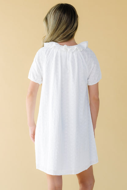 Back view of a woman wearing a white eyelet dress with short sleeves and a ruffled round collar.