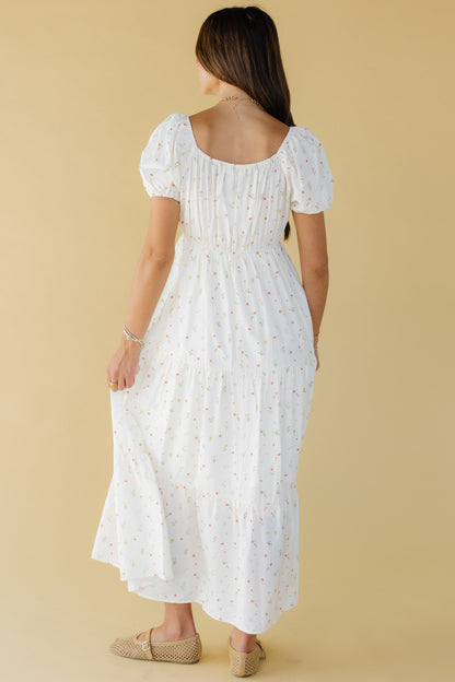 Back view of a woman wearing an off white midi dress with multiple gathered tiers, an elastic waistband, short puff sleeves and and elastic scoop back neckline.