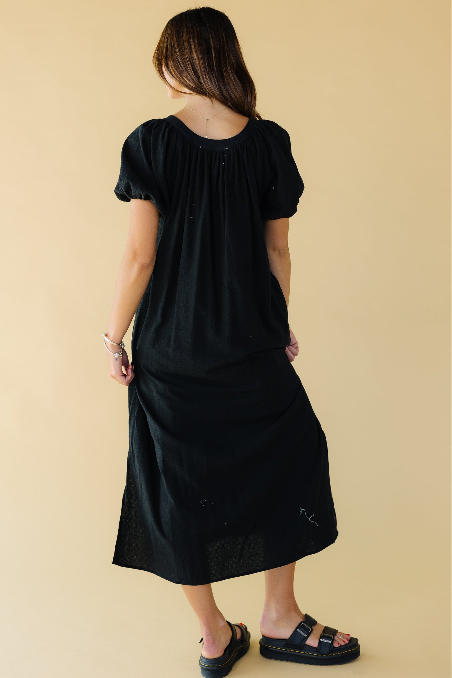 Back view of a woman wearing a black midi-maxi dress with balloon sleeves and a scoop neckline.
