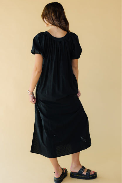 Back view of a woman wearing a black midi-maxi dress with balloon sleeves and a scoop neckline.