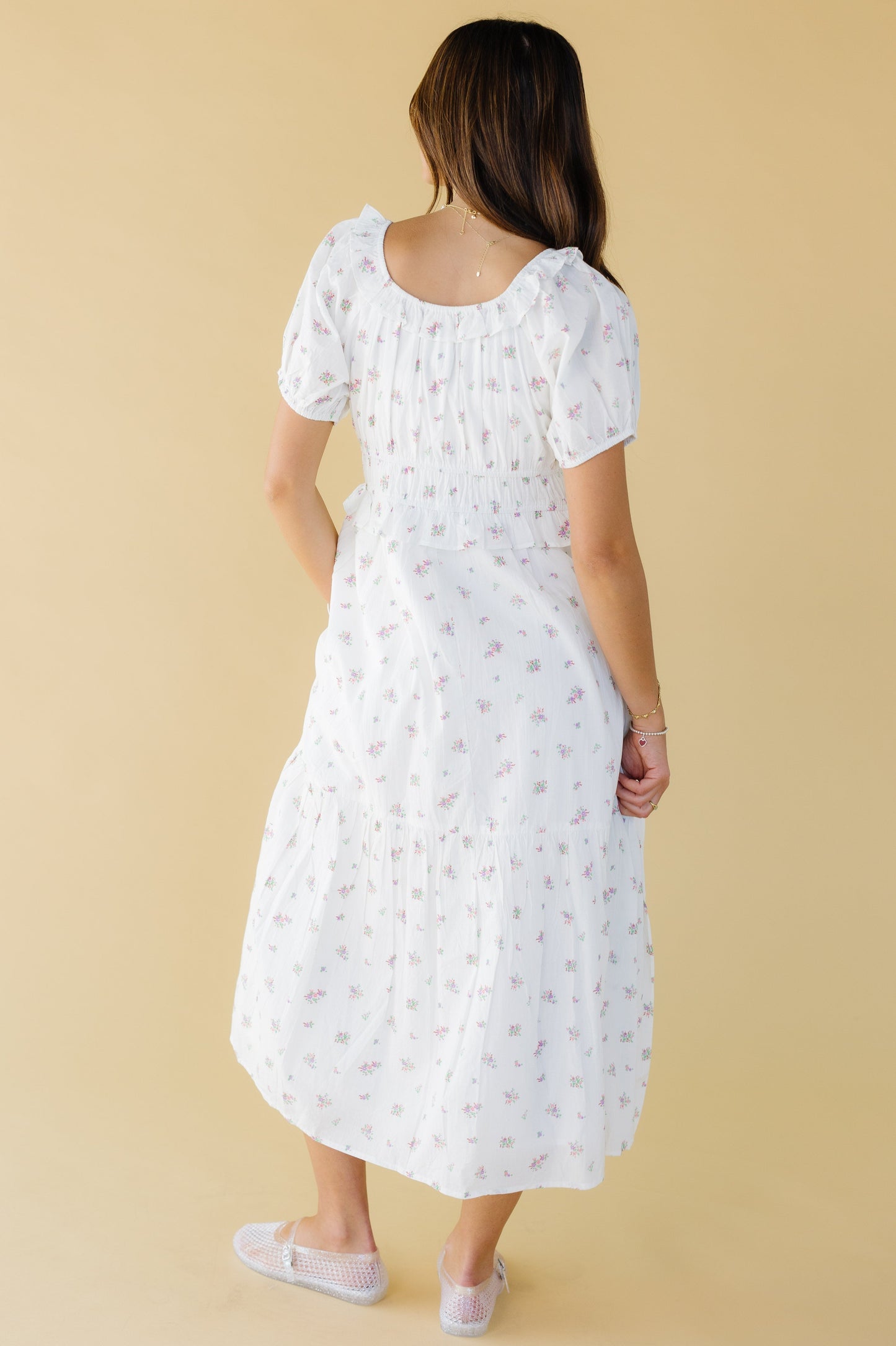 Back view of a woman wearing a white & pink floral midi-maxi dress with puff sleeves and a ruffled scoop back neckline.