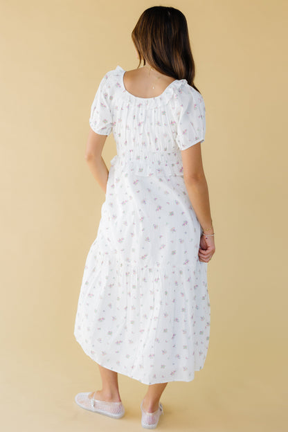 Back view of a woman wearing a white & pink floral midi-maxi dress with puff sleeves and a ruffled scoop back neckline.
