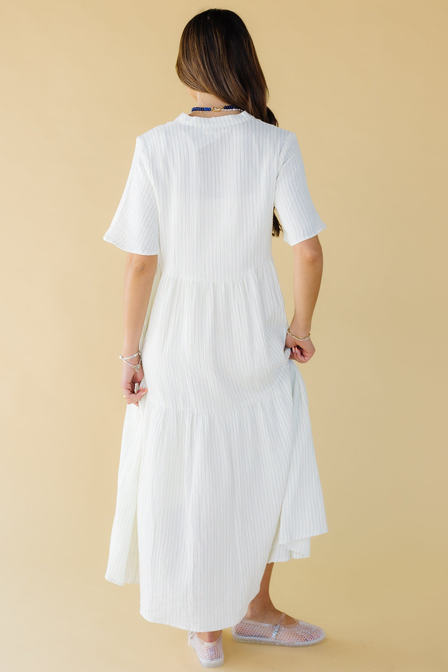 Back view of a woman wearing a white and blue stripe midi-maxi dress with short sleeves.