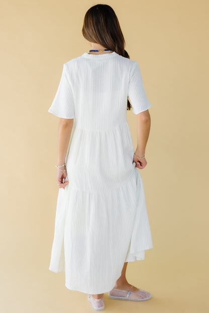 Back view of a woman wearing a white and blue stripe midi-maxi dress with short sleeves.