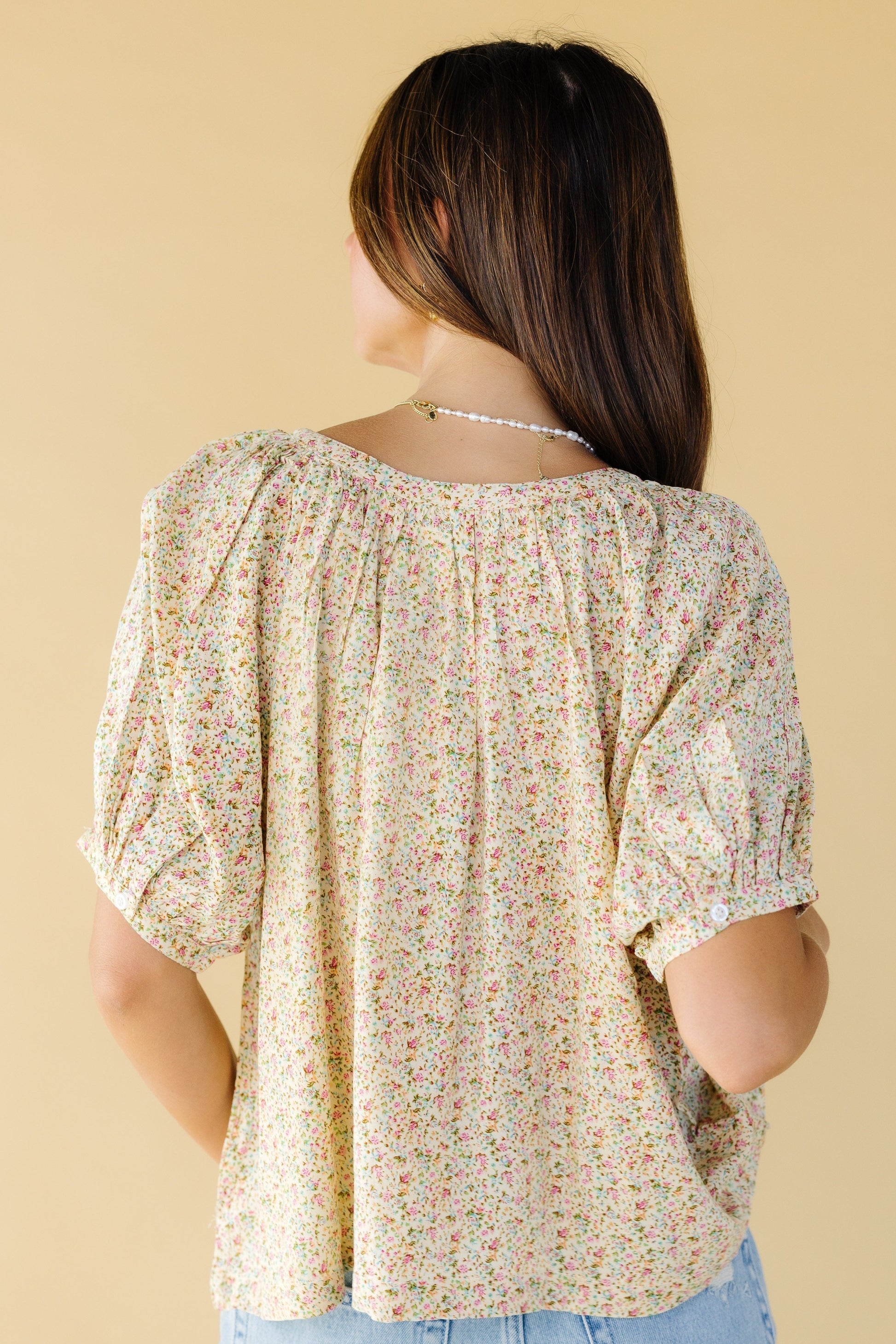 Back view of a young woman wearing a yellow floral loose fitting blouse.