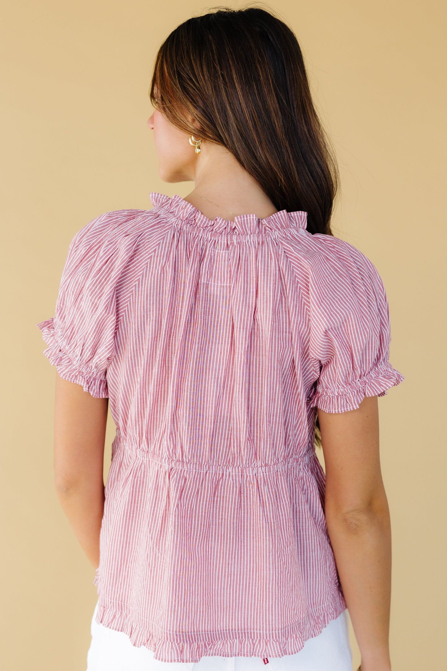 Back view of a woman wearing a red stripe top with a short puff sleeve and an elastic waist.
