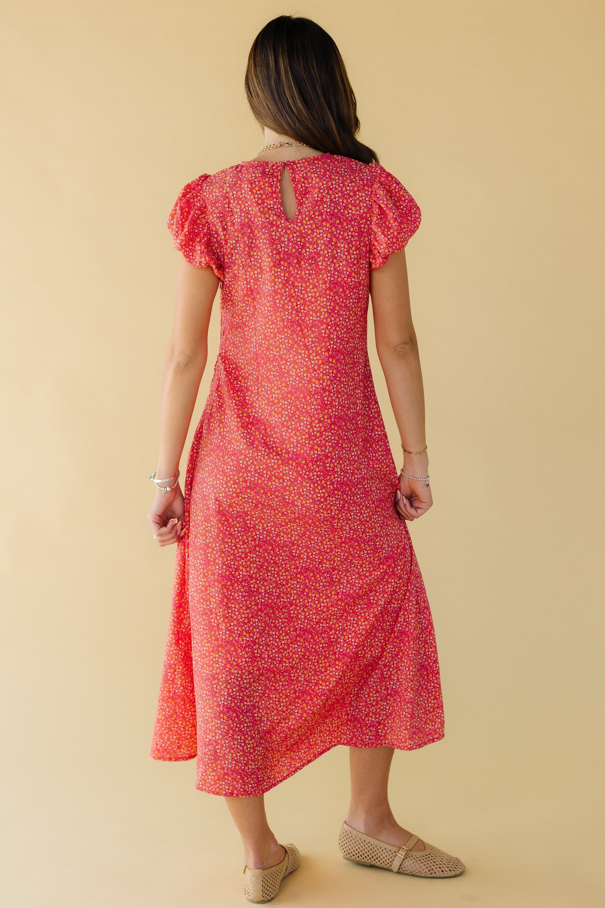 Back view of a young woman wearing a red floral midi dress with a button-keyhole closure with short puffy sleeves.