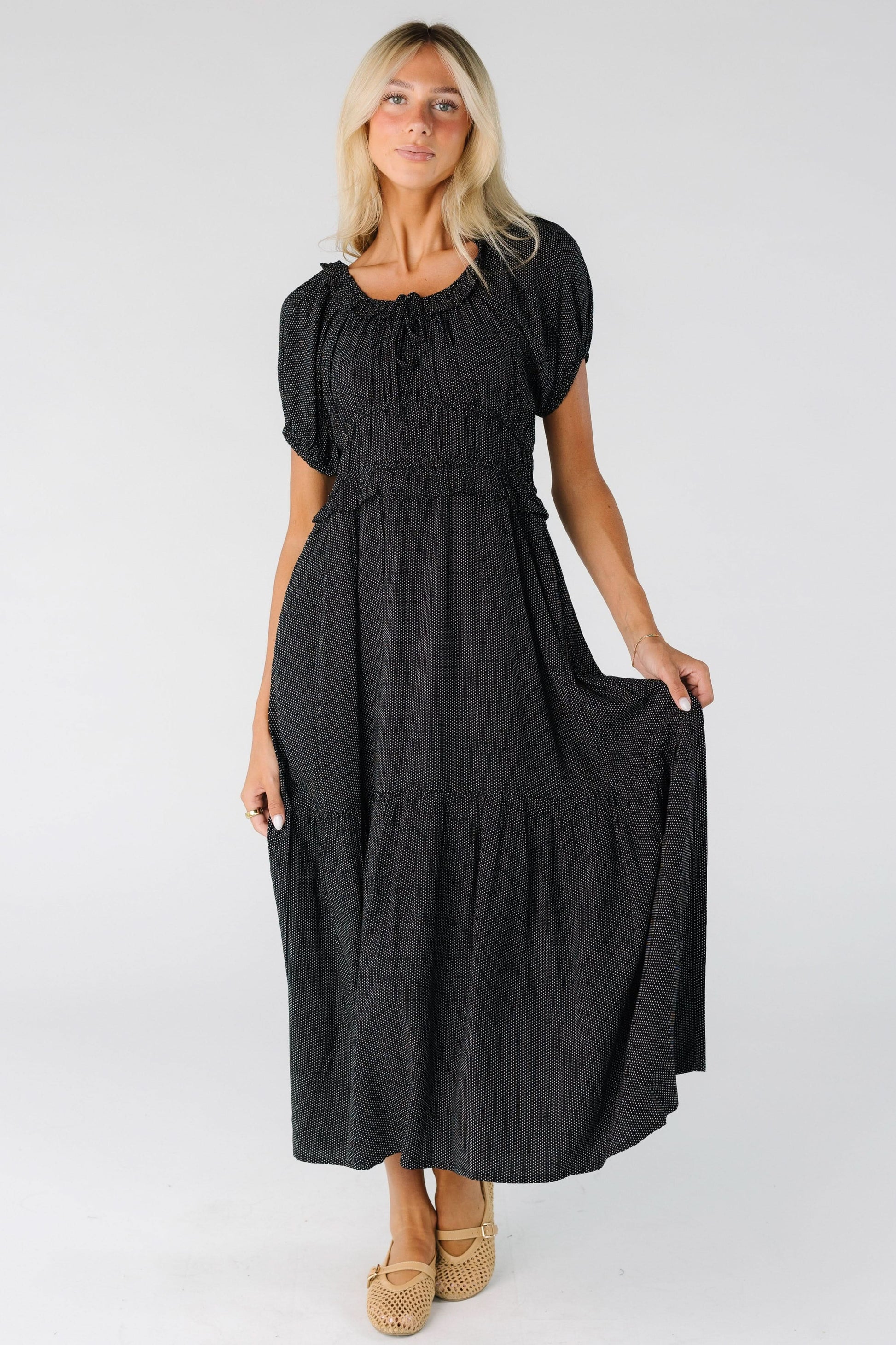 Young woman wearing a modest black polka dot midi dress with a wide bottom rufle, wide wasit with a ruffle, short sleeves and a scoop ruffled neckline and puff sleeves.