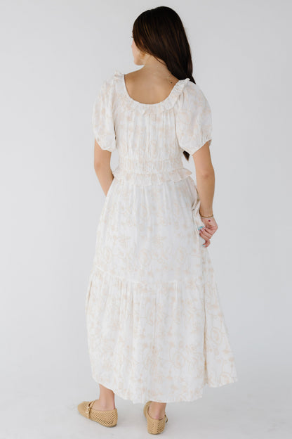 Back view of a young woman wearing a white embroidered midi-maxi dress with a wide waist and short puff sleeves.