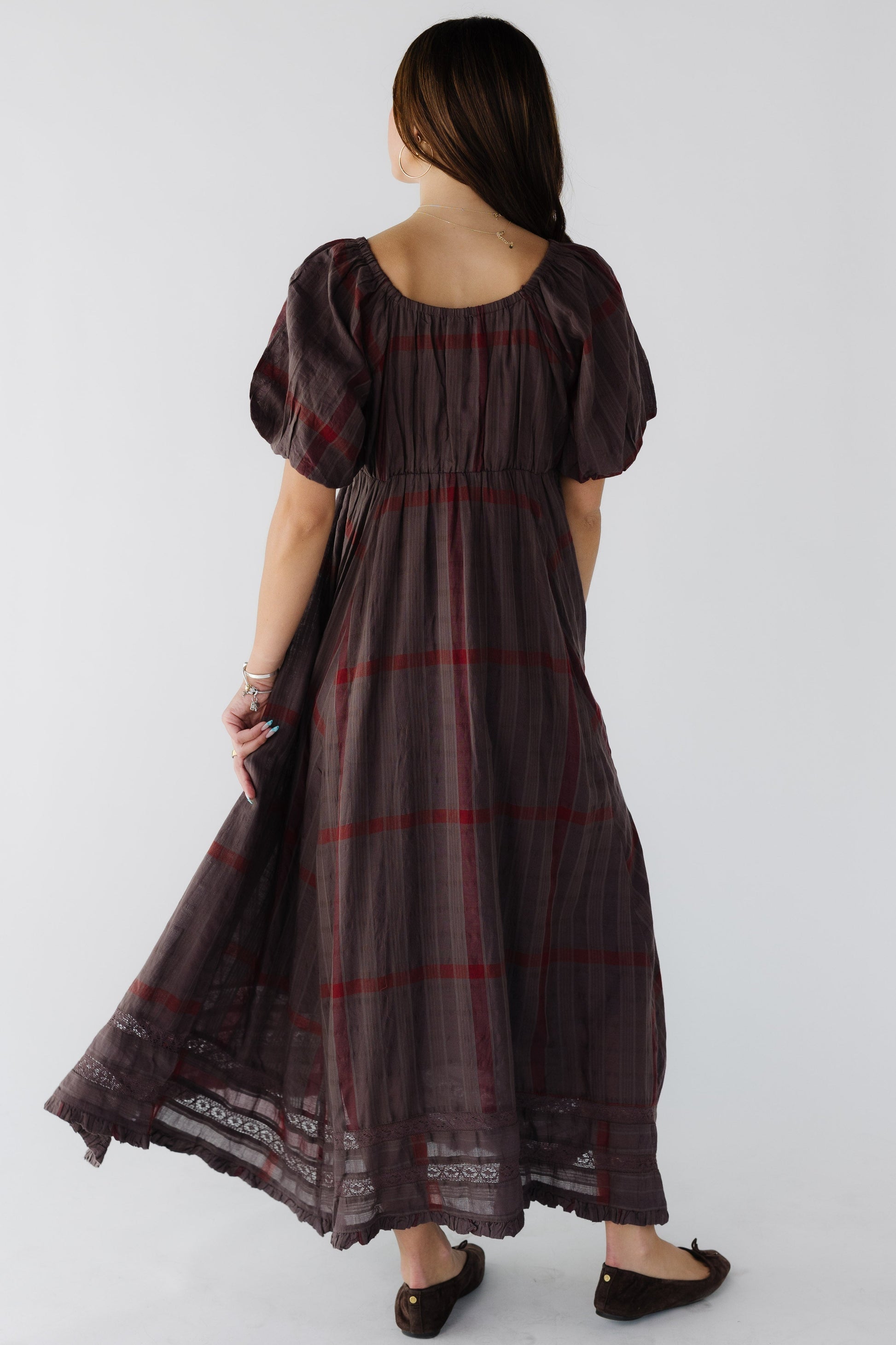 Back view of a woman wearing a brown & red plaid dress with a kerchief hemline, lace inset and a back scoot neckline with balloon sleeves.