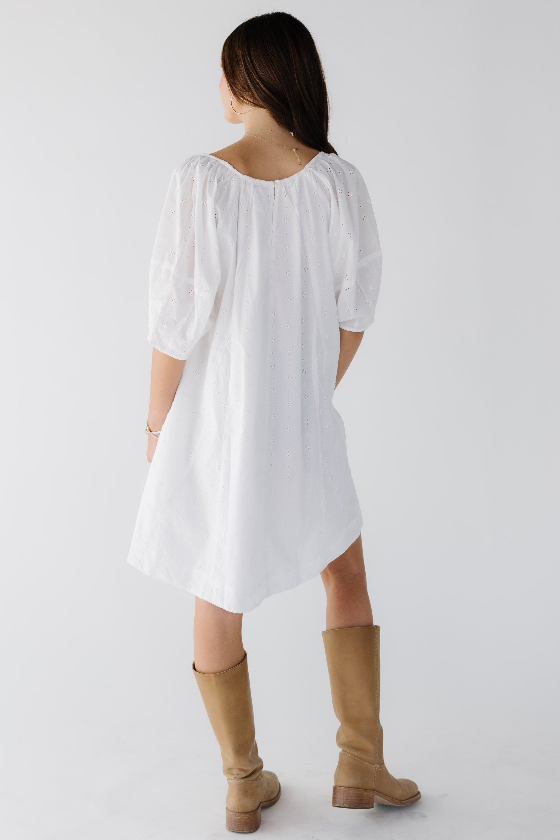 Back view of a woman wearing an all eyelet white short dress with elbow lenth sleeves.