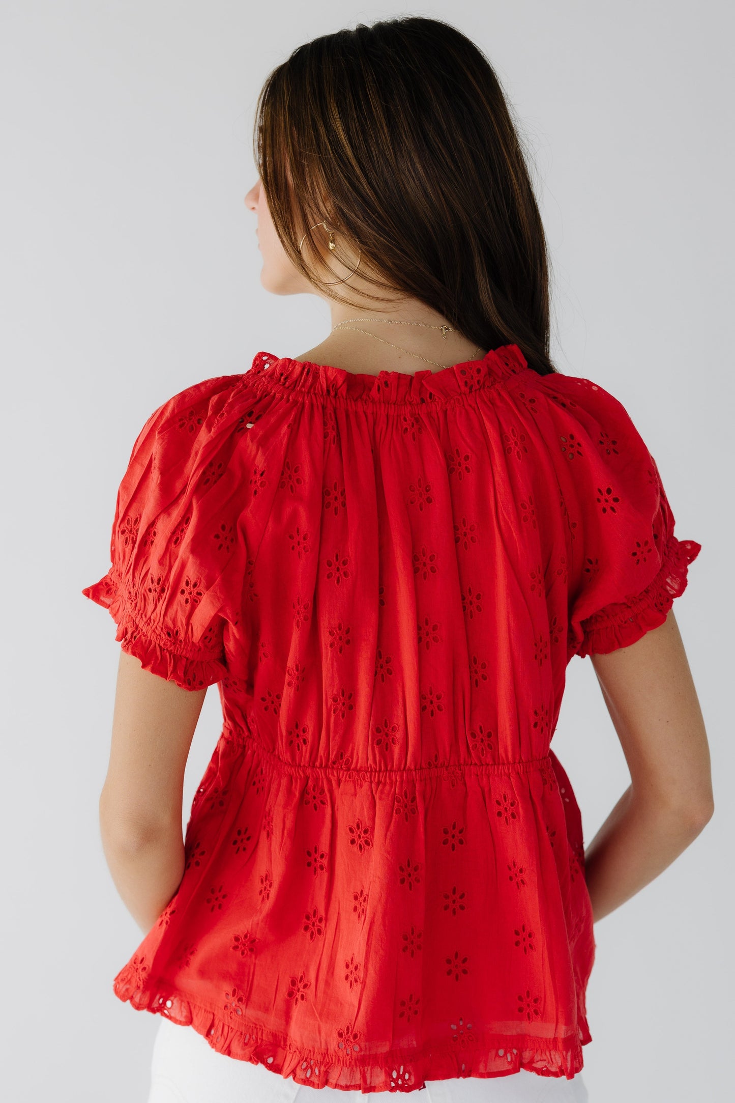 Back view of a woman wearing a red eyelet loose fittingbloue with short puff sleeves.
