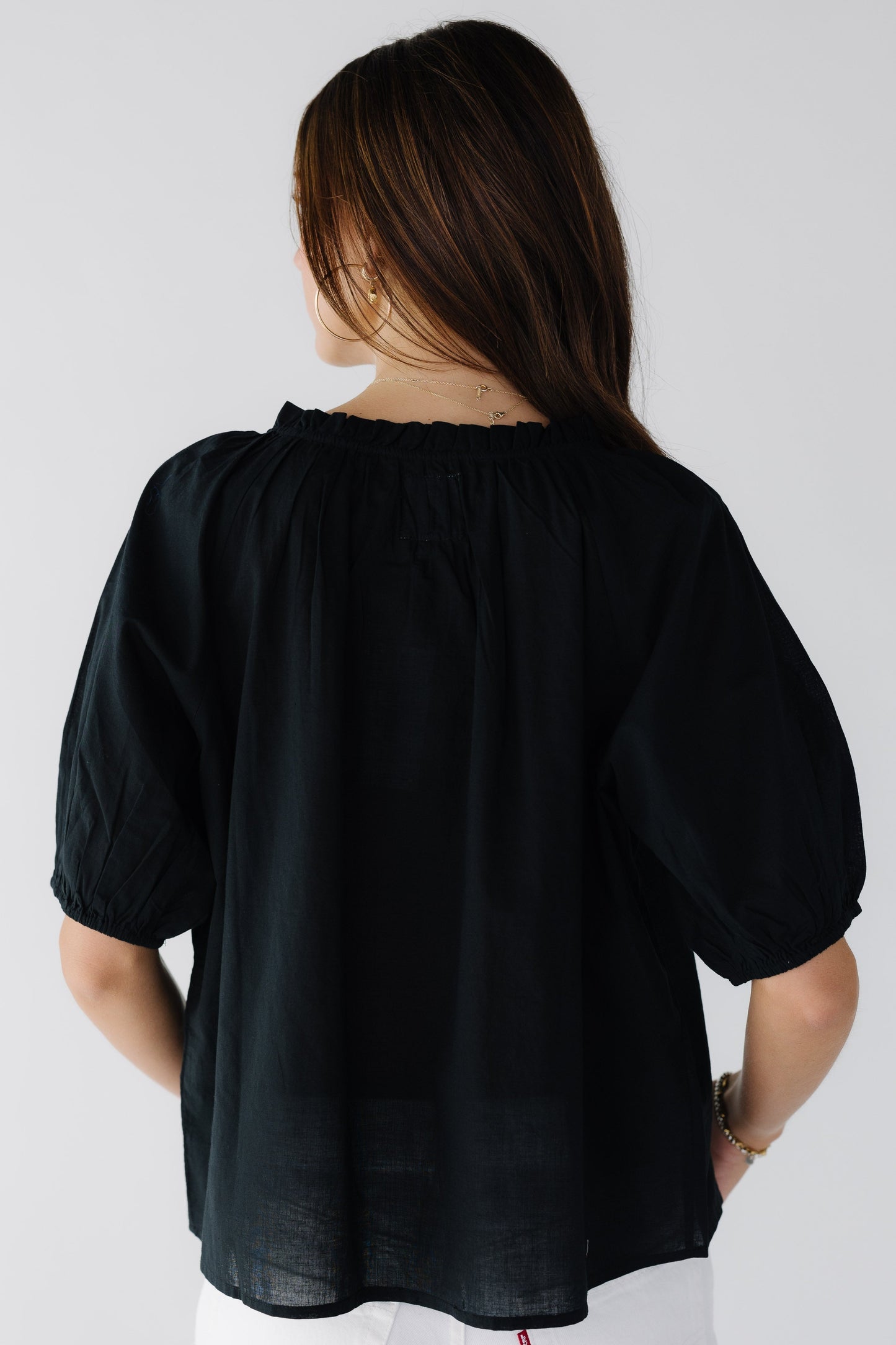 Back view of a young woman wearing a loose black top with gathered elbow length sleeves.