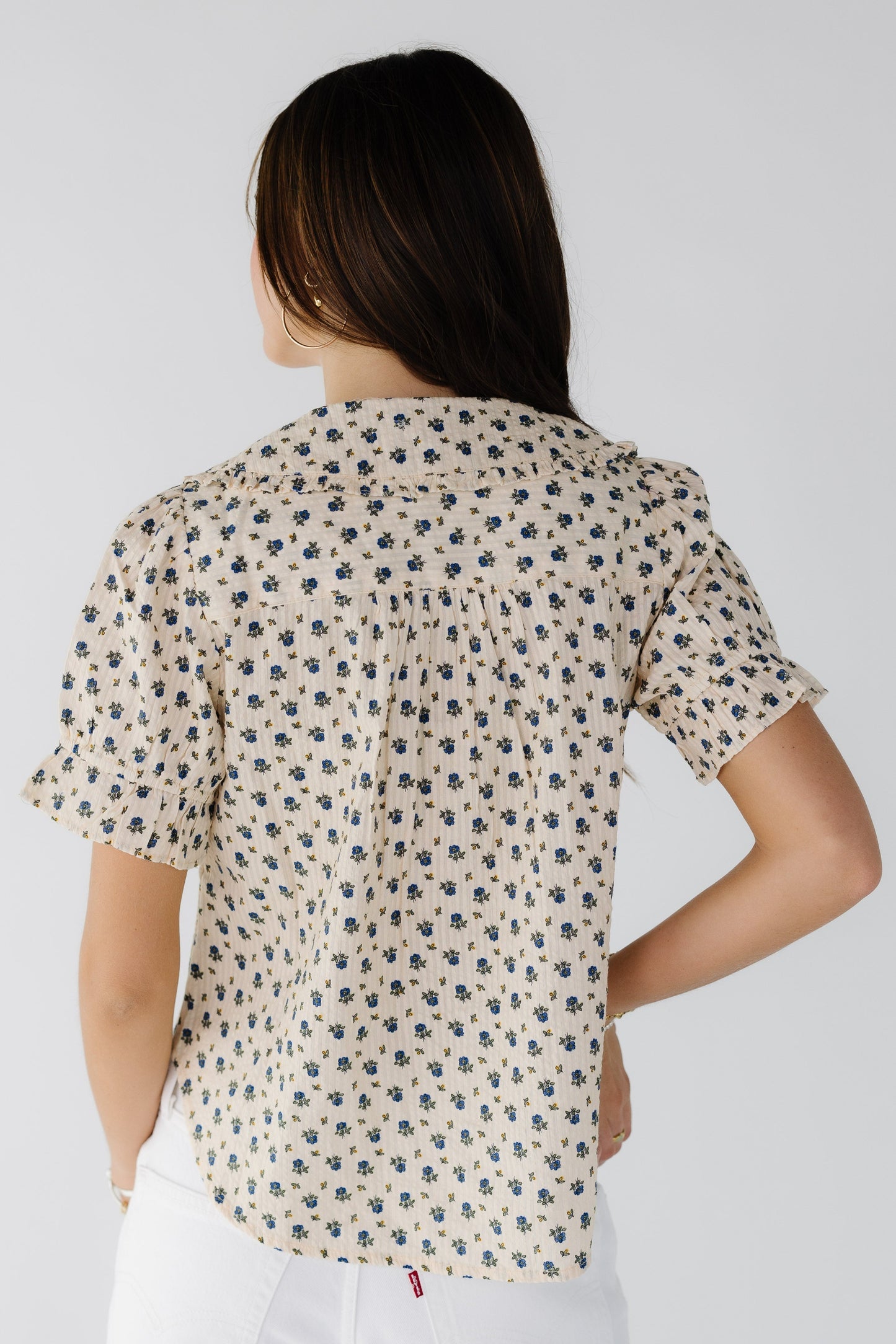 Back view of a woman wearing a cream and blue floral print blouse with short puff sleeves.
