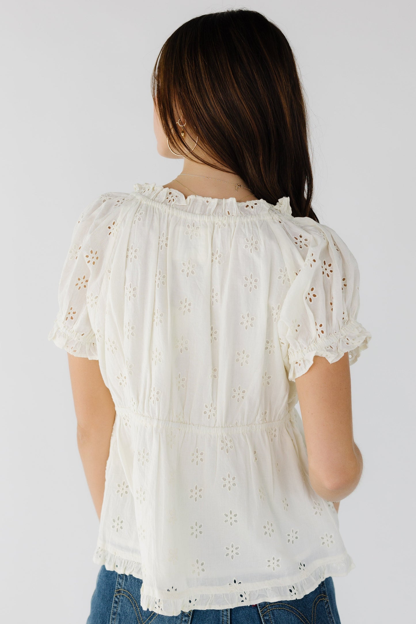 Back view of a young woman wearing a cream eyelet blouse with puff sleeves.