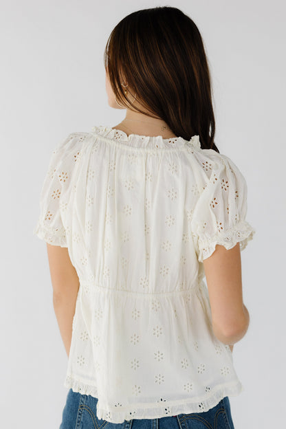 Back view of a young woman wearing a cream eyelet blouse with puff sleeves.