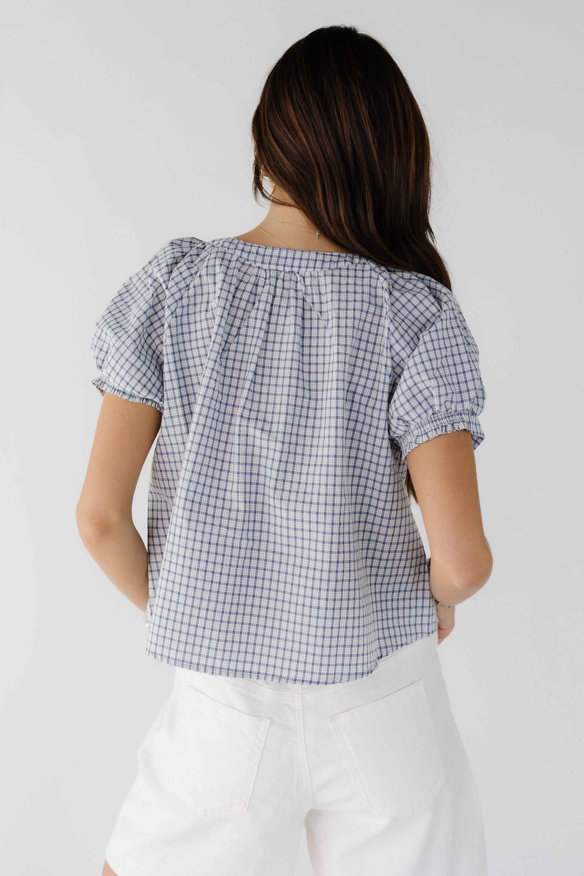 BAck view of a woman wearing a loose fitting blue & white plaid blouse with short puff sleeves.