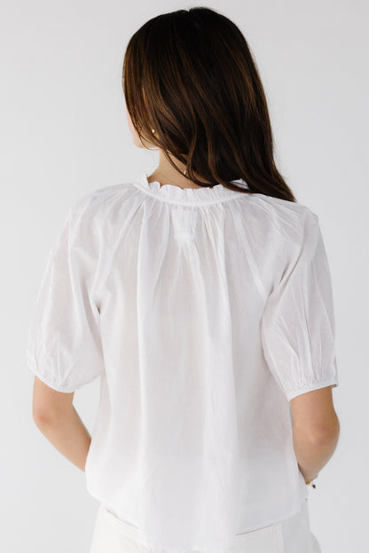 Back view of a young woman wearing a white loose fitting blouse with short gathered sleeves and a ruffled collar.