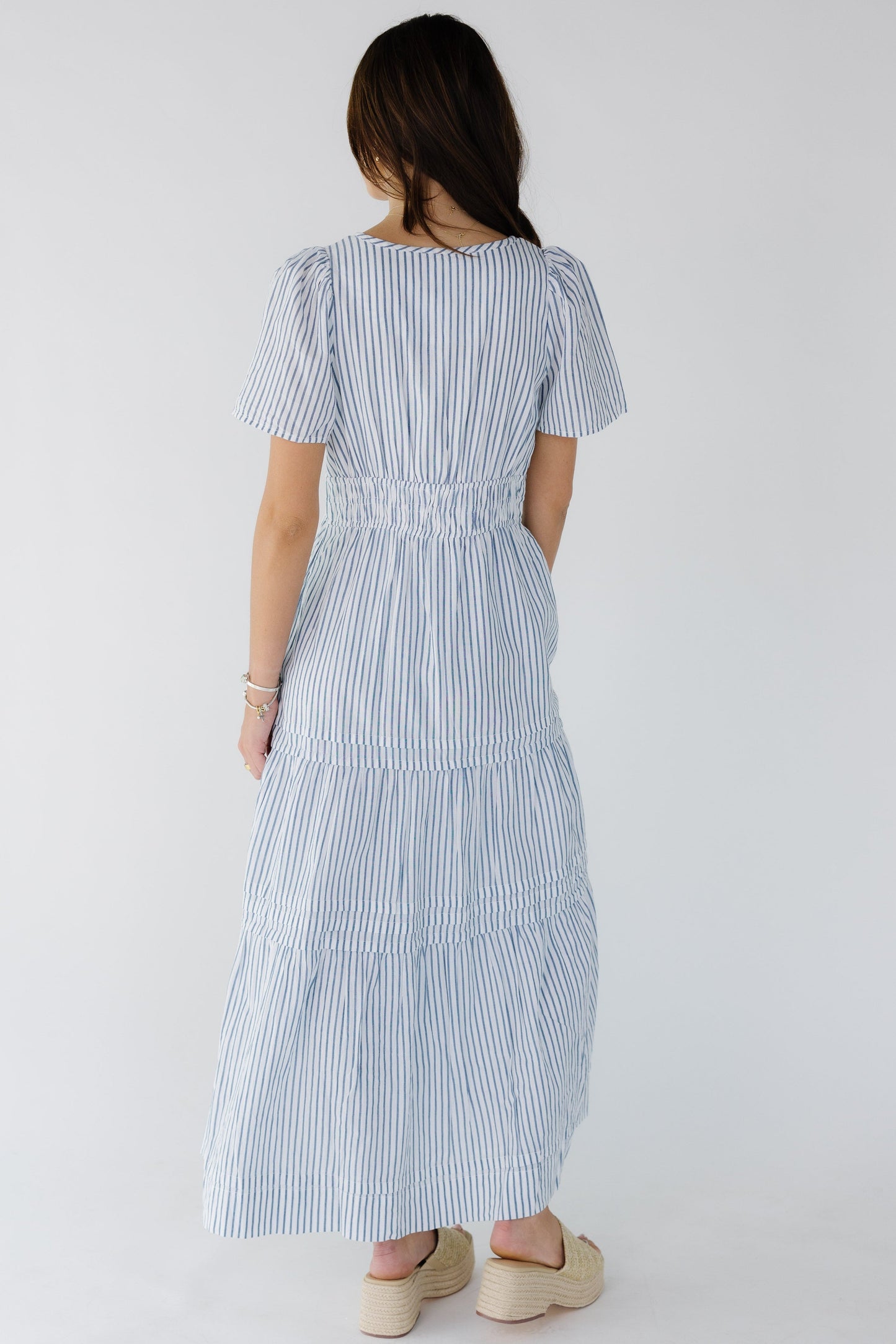 Back view of a young woman wearing a white and blue stripe with short sleeves.