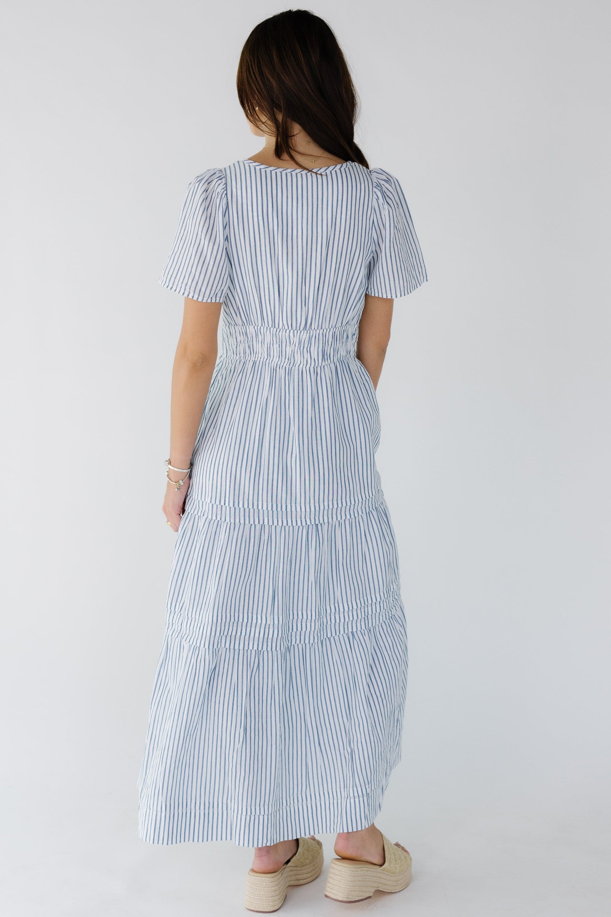 Back view of a young woman wearing a white and blue stripe with short sleeves.