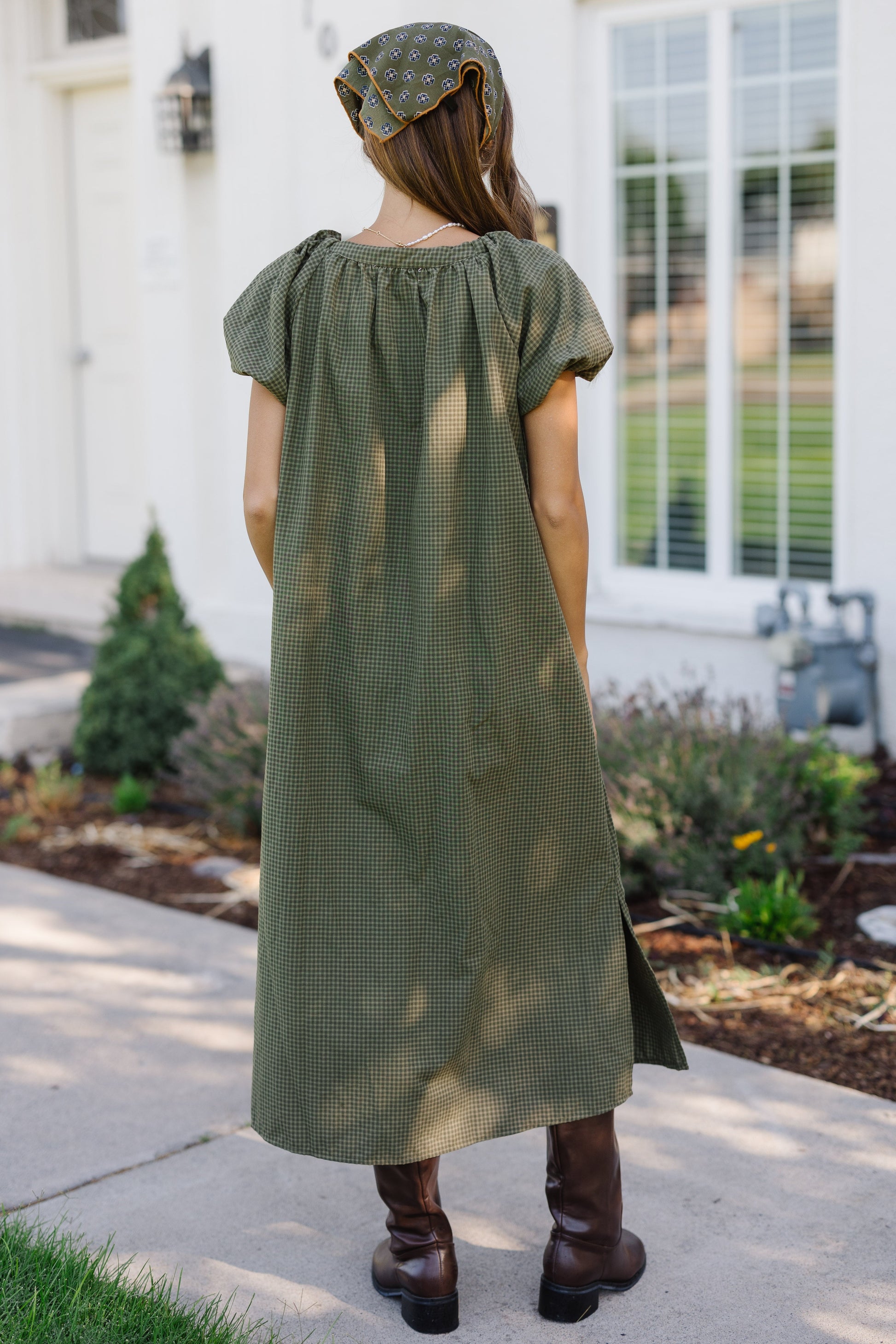 Back view of a woman wearing a loose fitting green gingham midi dress with puff sleeves.