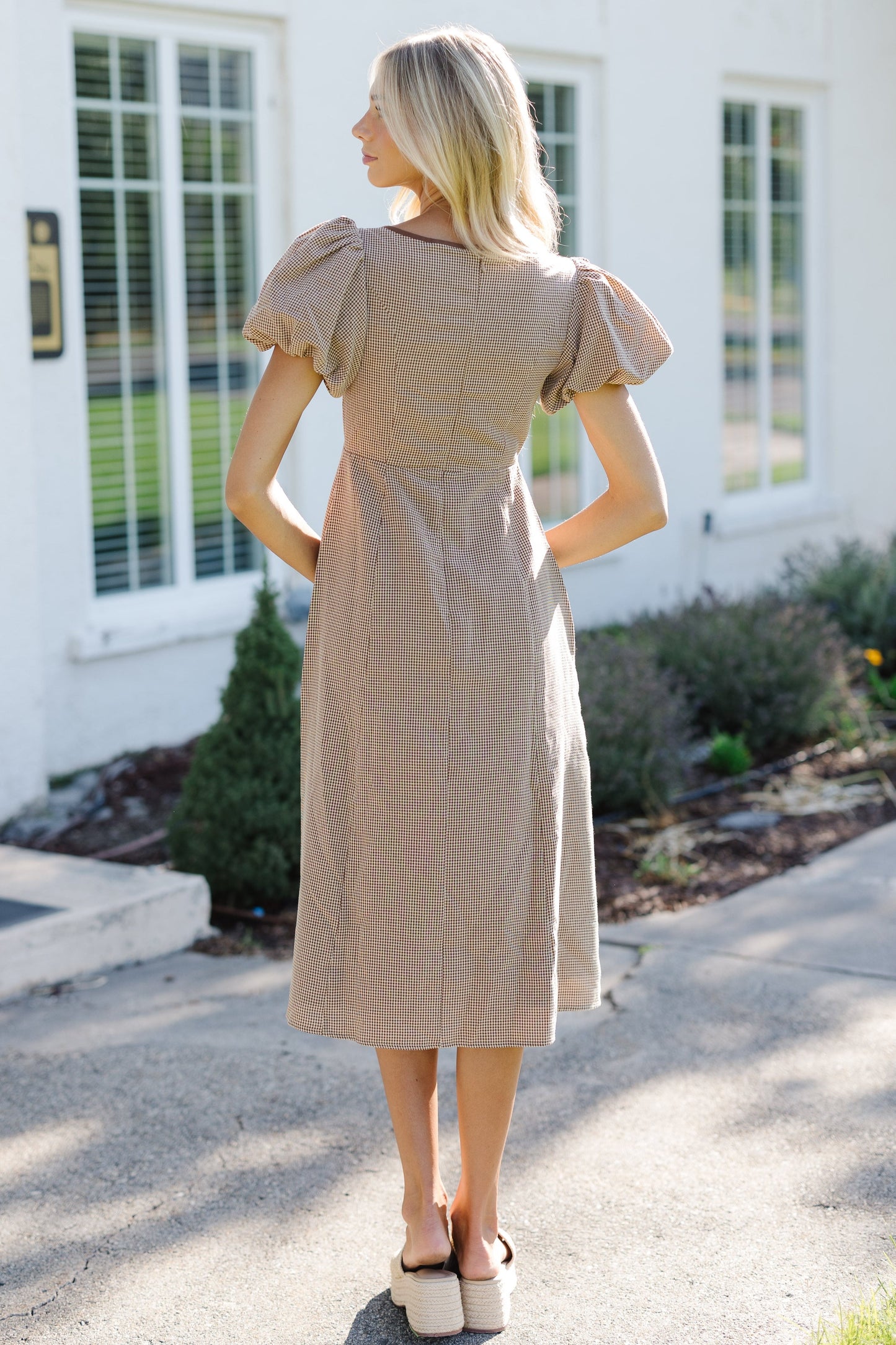 Woman wearing a brown gingham midi dress with an A-line skirt, close fitting bodice and balloon sleeves.