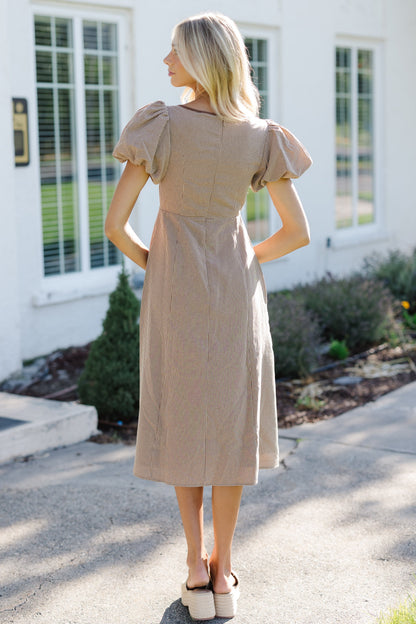 Woman wearing a brown gingham midi dress with an A-line skirt, close fitting bodice and balloon sleeves.