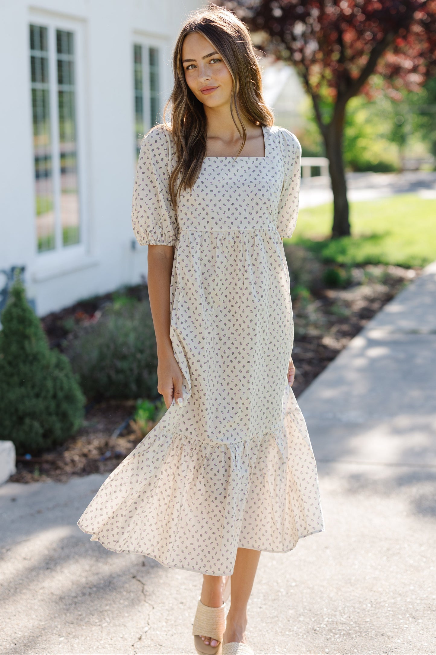 Woman wearing a cream print midi dress of short puff sleeves and a square neckline.