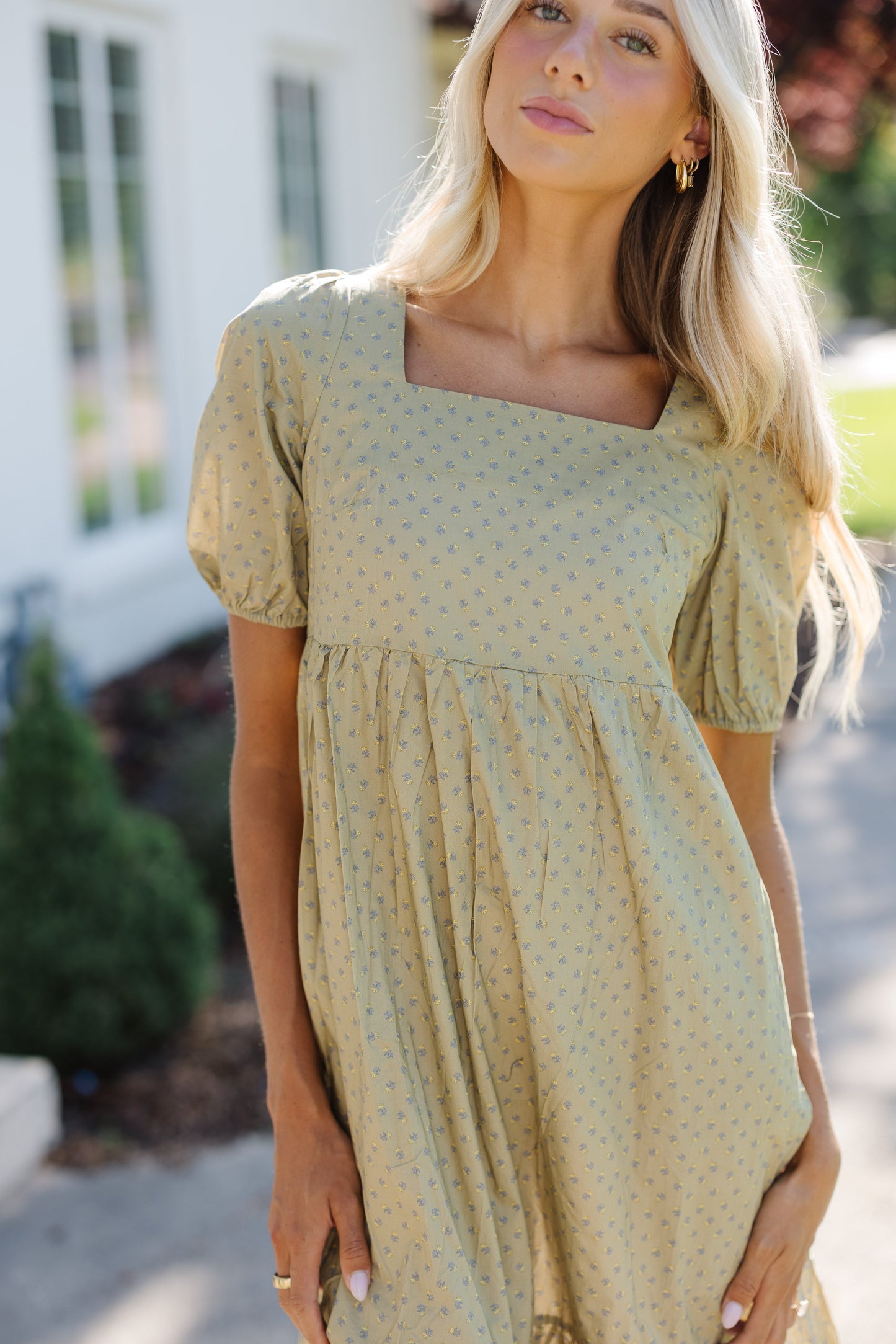 Close view of a woman wearing an square neck olive print dress with large puff sleeves and gathered waist.