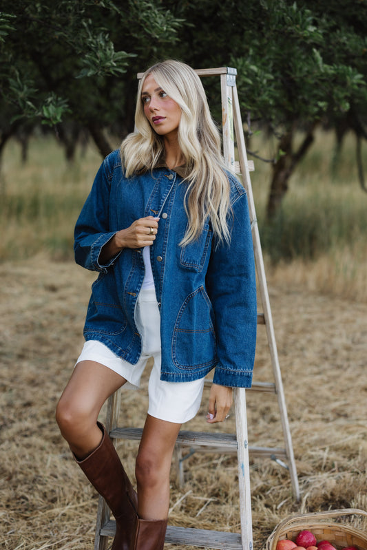 Young woman wearing a modest long denim jacket with long sleeves, corduroy pointd collar and metal buttons.