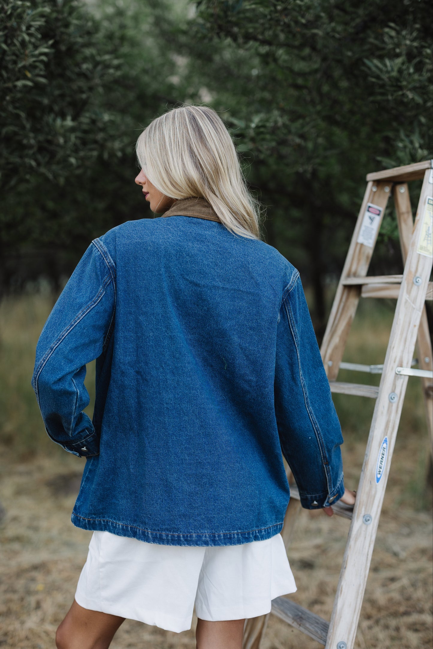 Back view of a young woman wearing a loose fitting denim jacket in mid hip length.