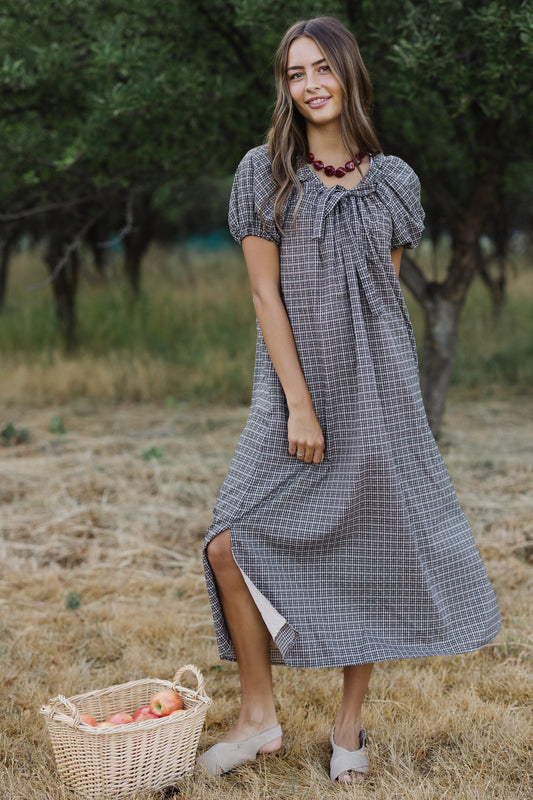 Young woman wearing a modest black plaid loose fitting midi dress with large puff sleeves and side slits. 
