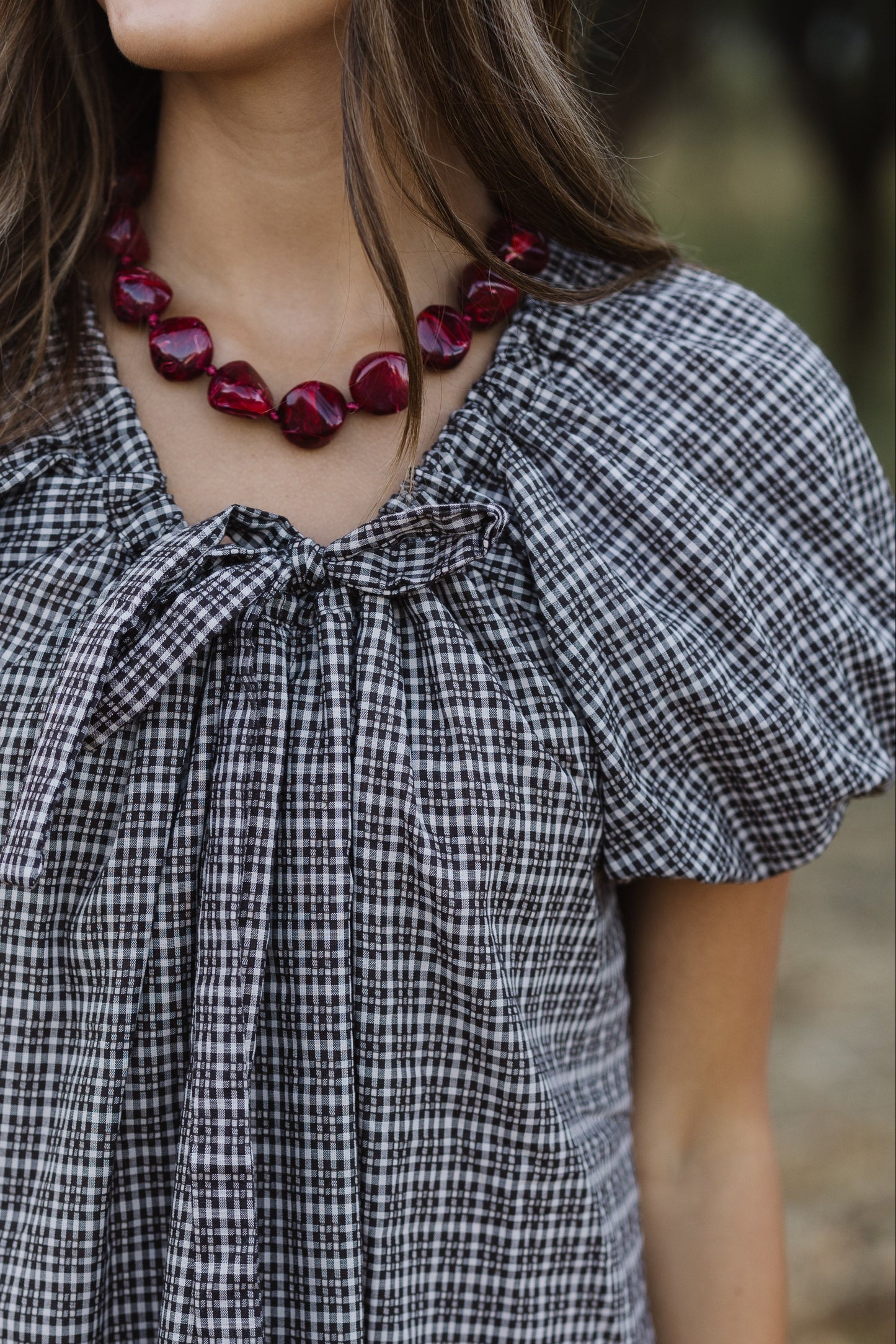 Close view of a woman wearing a black plaid dress with large puff sleeves and a drawstring-scoop neckline.