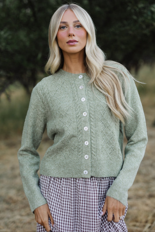 Young woman weabuttonring a modest light green cable knit button cardigan wigh long sleeves.