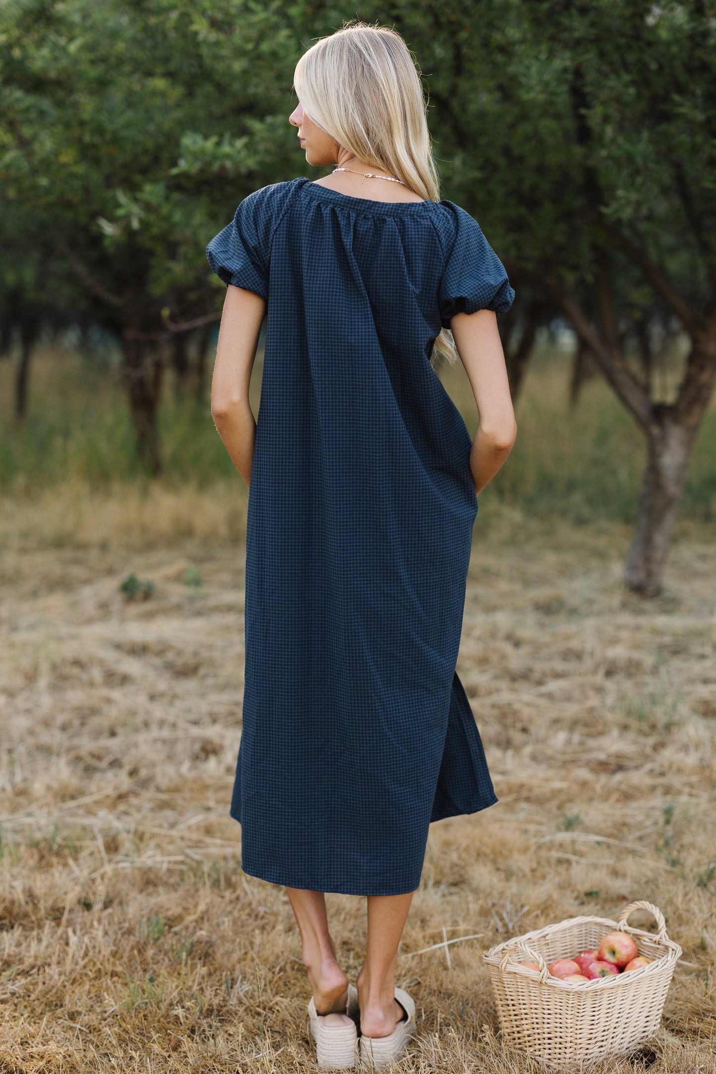 Back view of a woman wearing a loose fitting midi dress in avy gingham and short puff sleeves.